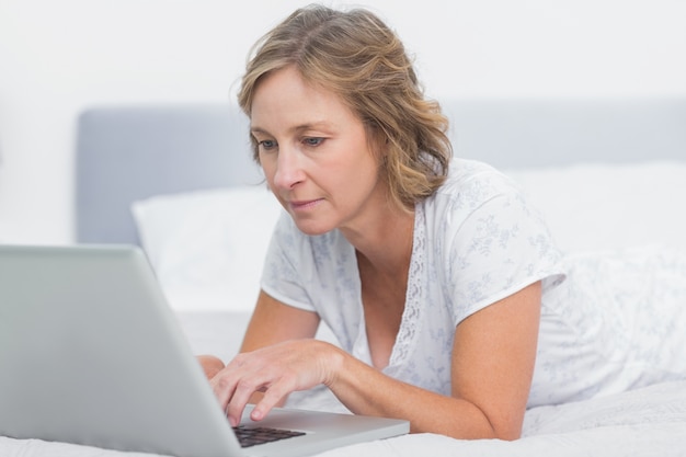 Donna bionda seria che si trova sul letto facendo uso del computer portatile