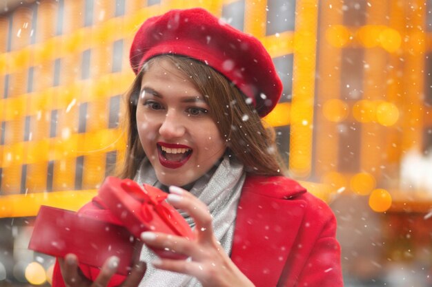 Donna bionda sorpresa che riceve una confezione regalo rossa a forma di cuore per strada durante la nevicata. Spazio vuoto