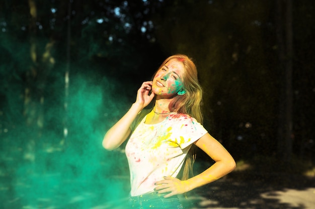 Donna bionda sorridente che gioca con la vernice secca verde Holi nel parco
