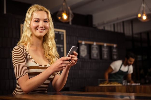 Donna bionda sorridente che per mezzo dello smartphone