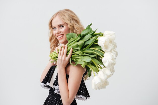 Donna bionda sorridente che posa con il mazzo dei fiori