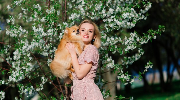 Donna bionda sorridente con il suo cane di Pomerania nel parco