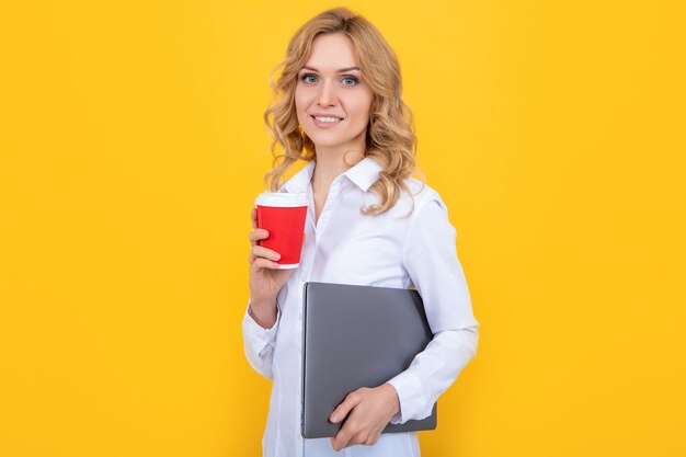 Donna bionda sorridente con tazza di caffè e laptop su sfondo giallo