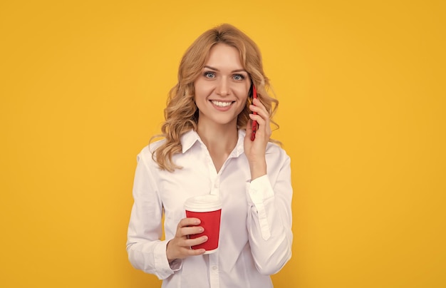 Donna bionda sorridente con una tazza di caffè che parla al telefono su sfondo giallo