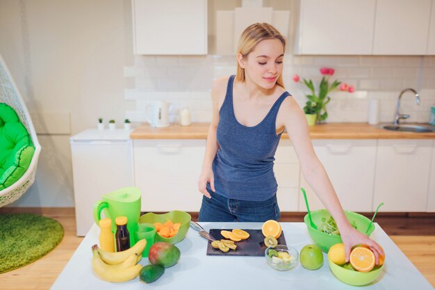 Donna bionda sorridente dei giovani che cucina frutta fresca nella cucina