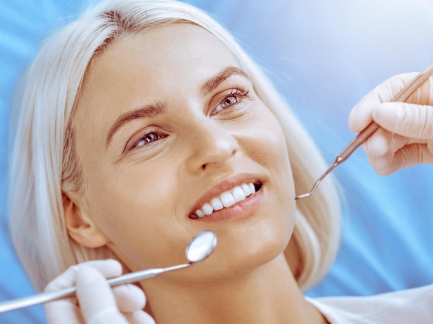 Donna bionda sorridente esaminata dal dentista presso la clinica odontoiatrica. Denti sani nel concetto di medicina.