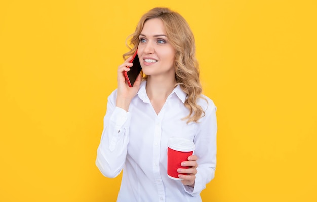 Donna bionda sorriso con tazza di caffè parlando al telefono su sfondo giallo