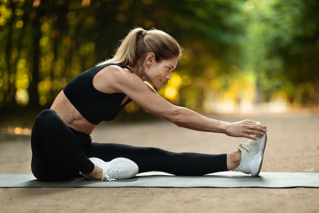 Donna bionda sportiva che si estende sulla stuoia di yoga al parco