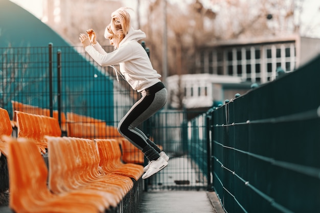 Donna bionda sportiva esile in abiti sportivi che salta sul sedile