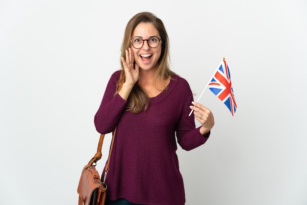 Donna brasiliana di mezza età che tiene una bandiera del Regno Unito isolata sul muro bianco che grida con la bocca spalancata