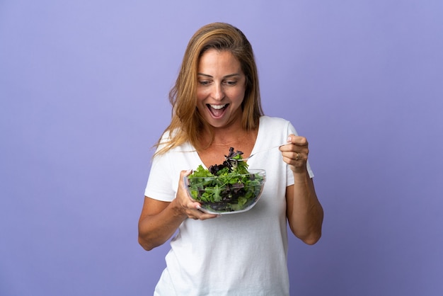 Donna brasiliana di mezza età isolata su che tiene una ciotola di insalata con l'espressione felice