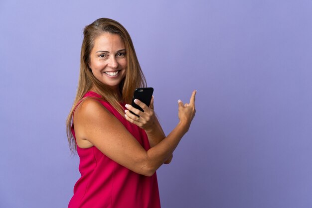 Donna brasiliana di mezza età isolata su viola utilizzando il telefono cellulare e rivolto indietro