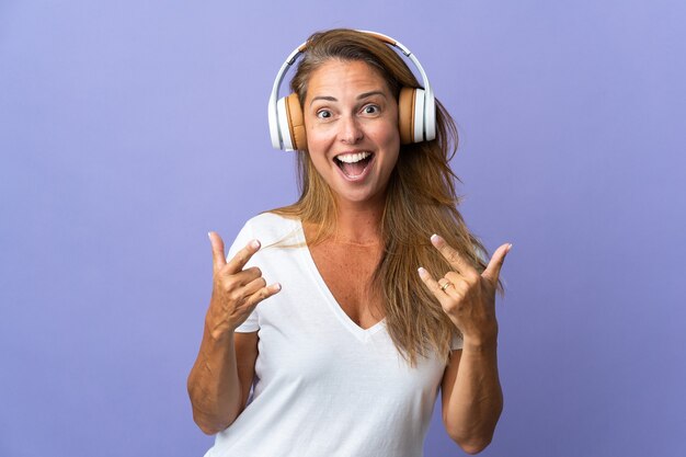 Donna brasiliana di mezza età isolata sulla musica d'ascolto viola che fa gesto della roccia