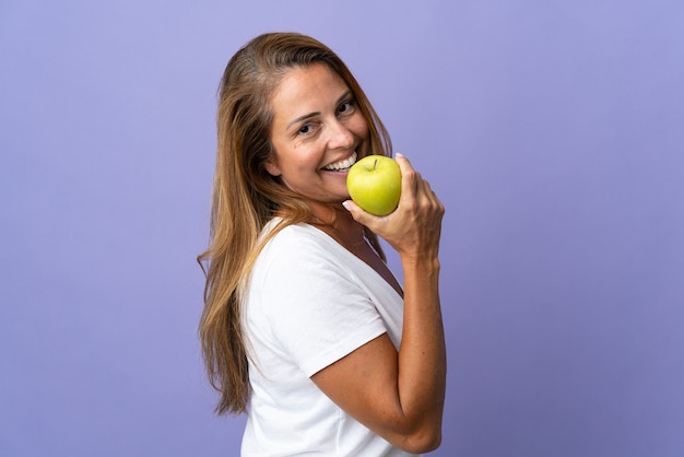 Donna brasiliana di mezza età isolata sulla parete viola che mangia una mela