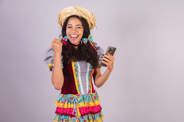 Donna brasiliana nera che indossa abiti da festa di giugno fraternizzazione in nome di Sao Joao Arraial con lo smartphone