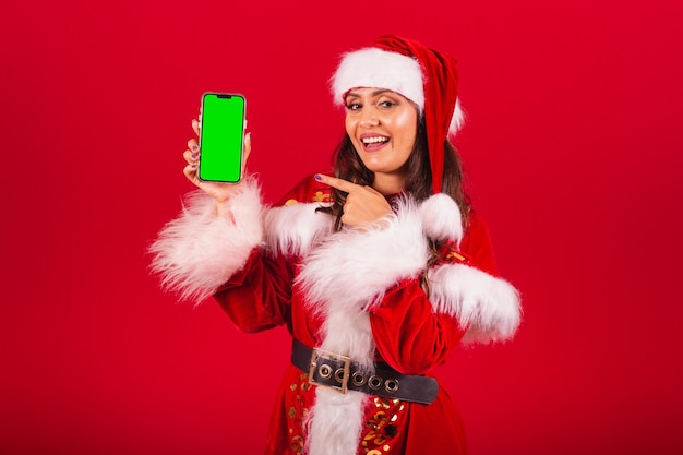 Donna brasiliana vestita con abiti natalizi Babbo Natale che tiene smartphone con schermo verde in chroma
