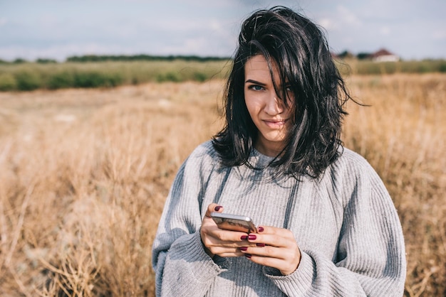 Donna bruna caucasica che utilizza lo smartphone per inviare messaggi di testo e connessione wireless per la vita sociale sullo sfondo della natura con capelli ventosi, sorriso e sentirsi liberi Spazio di copia Concetto di persone