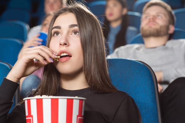 donna bruna che mangia popcorn mentre si guarda film al cinema locale