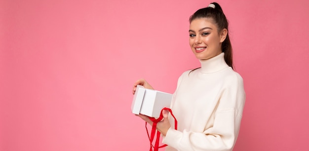 donna bruna isolato su sfondo rosa muro indossa un maglione bianco azienda confezione regalo