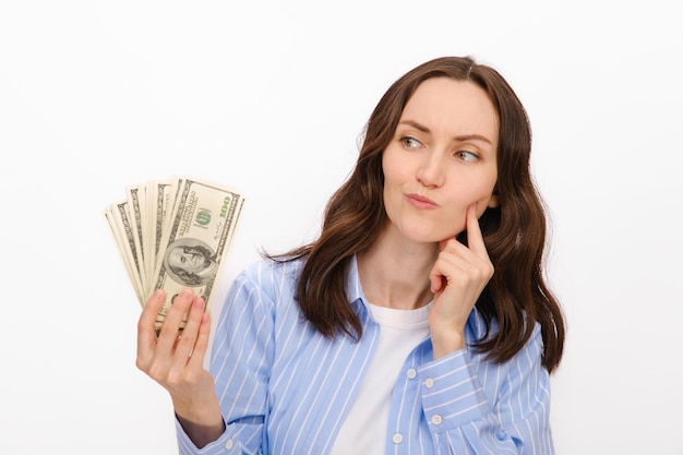 Donna bruna premurosa in camicia blu guarda i dollari nelle sue mani su sfondo bianco