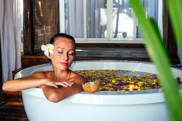 Donna bruna sexy che si rilassa nella vasca da bagno con fiori tropicali all'aperto presso il resort di hotel di lusso Cura della pelle organica Bella ragazza che riposa nel massaggio termale dell'hotel e giorno delle donne di meditazione 8 marzo