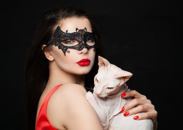 Donna bruna sexy con maschera di carnevale trucco labbra rosse e gatto glabro su sfondo nero Concetto di Halloween