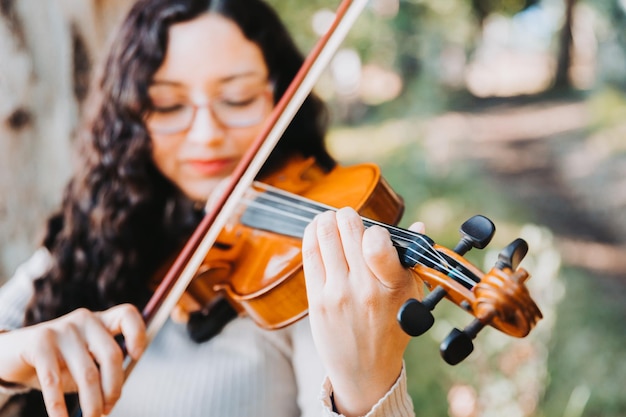 Donna bruna sorridente con occhiali suonare il violino fuori nel bosco Messa a fuoco selettiva