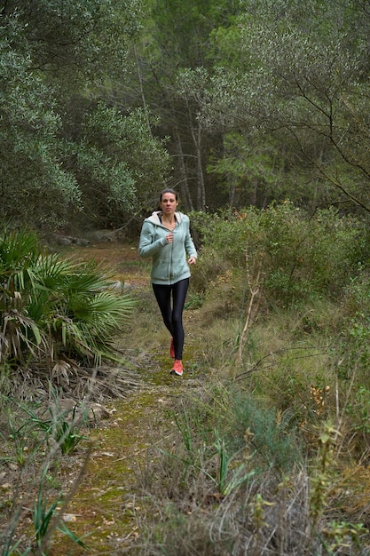 Donna bruna sportiva che corre attraverso la foresta in vista frontale di abbigliamento sportivo