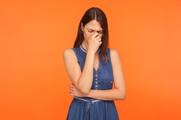 Donna bruna triste frustrata in abito di jeans che piange, si asciuga le lacrime, si sente depressa impotente, sconvolta per la perdita, il lutto, le emozioni disperate. tiro in studio indoor isolato su sfondo arancione