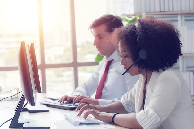 Donna call center Afroamericano che indossa abiti da lavoro bianchi con auricolare che lavora nel call center al computer