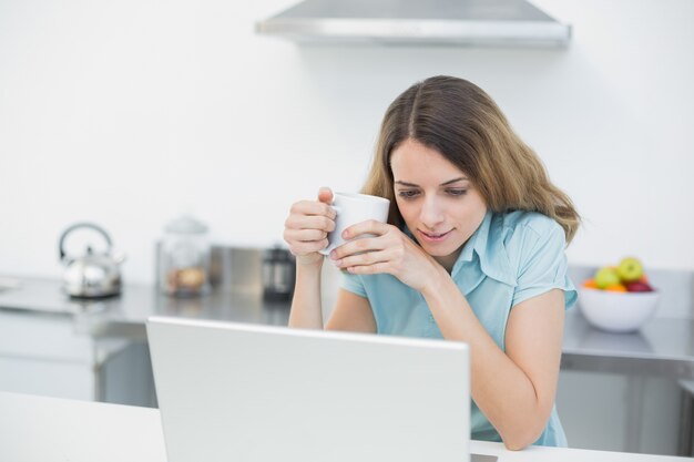 Donna calma carina che lavora con il suo taccuino che tiene una tazza