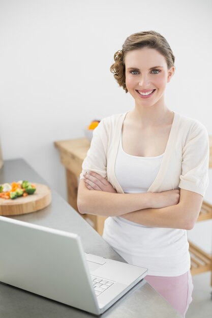 Donna calma contenta che posa nella sua cucina con le armi attraversate