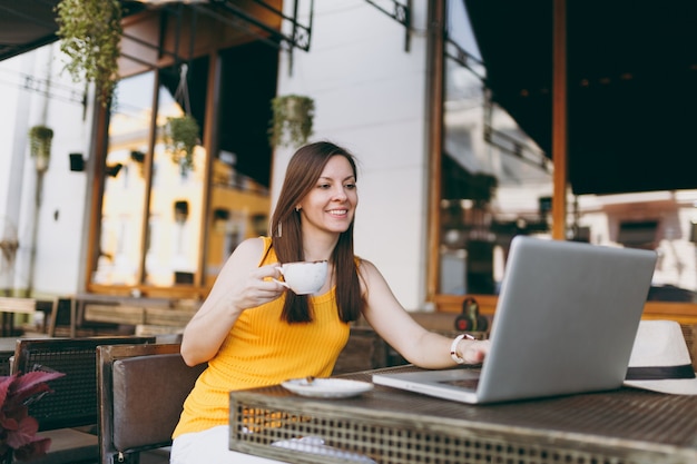 Donna calma nella caffetteria all'aperto di strada seduta al tavolo lavorando su un moderno computer portatile, bere una tazza di tè, rilassarsi al ristorante durante il tempo libero