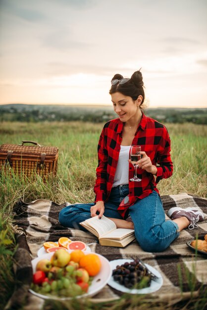 Donna carina con un bicchiere di vino legge il libro, picnic sul prato. Giostra romantica, buone vacanze