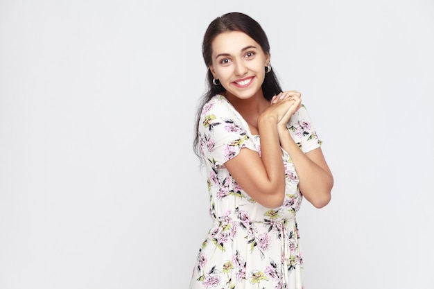 Donna carina e felice in abito di fiori, che guarda l'obbiettivo e sorriso a trentadue denti. Foto in studio, sfondo grigio