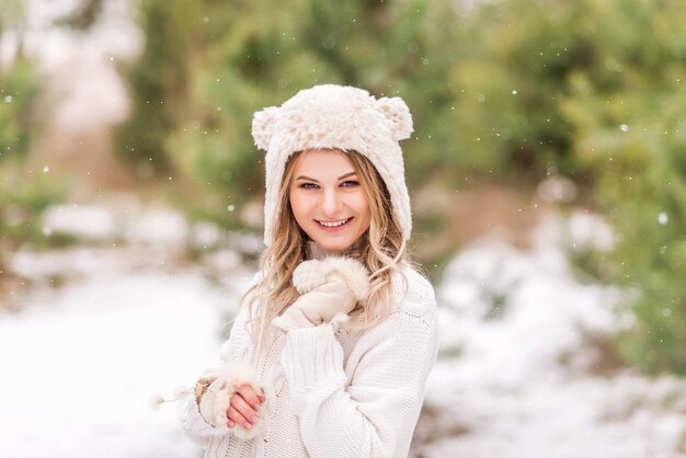 Donna carina in un maglione bianco e un buffo cappello nella foresta invernale