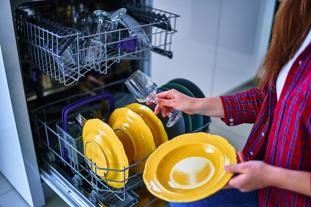 Donna casalinga che utilizza una moderna lavastoviglie per lavare piatti e bicchieri nella cucina di casa