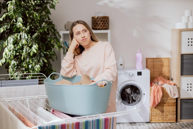 Donna casalinga stanca delle faccende domestiche ragazza in pantaloni della tuta si trova nella lavanderia accanto ai vestiti