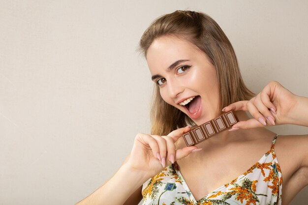 Donna castana adorabile allegra che tiene una piccola barra di cioccolato su un fondo grigio dello studio. Spazio vuoto