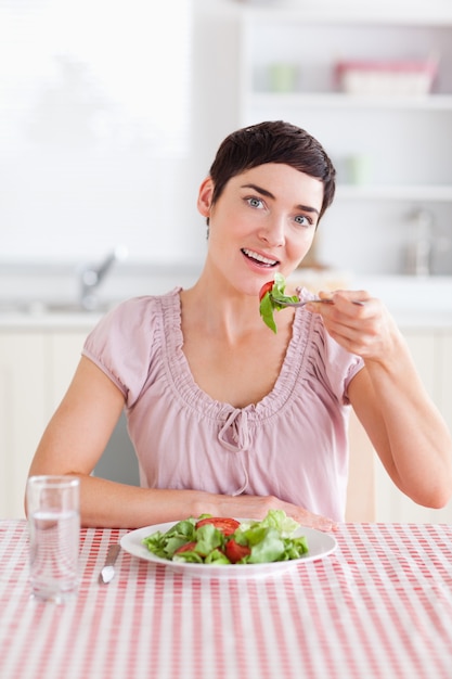 Donna castana allegra che mangia insalata