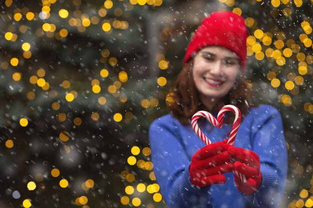 Donna castana allegra con la caramella all'albero di Natale durante la nevicata. Spazio per il testo