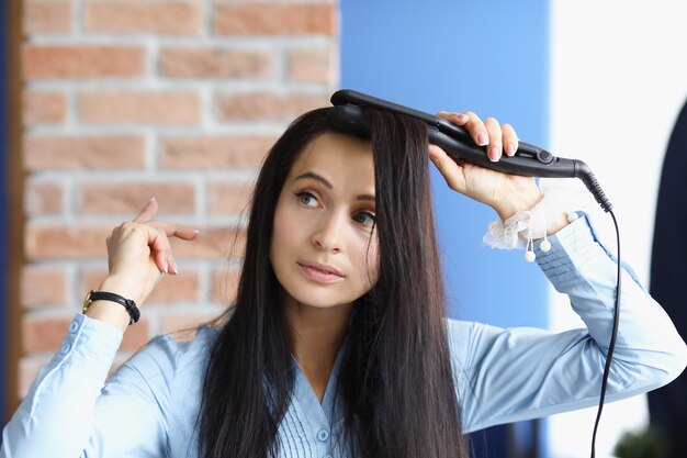 Donna castana arriccia i capelli con il ferro arricciacapelli