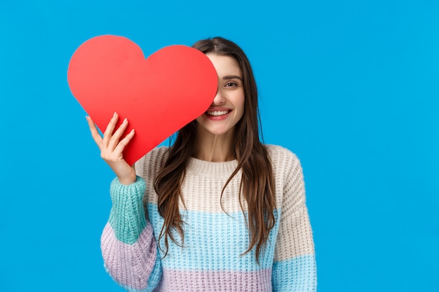 donna castana che tiene cuore rosso e che copre il suo fronte