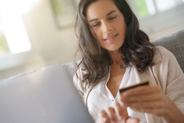 Donna castana collegata con il computer portatile, acquistante in linea