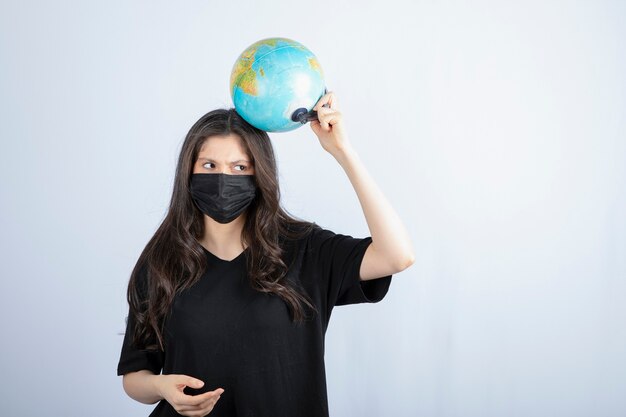 Donna castana con capelli lunghi nella mascherina medica che tiene il globo del mondo.