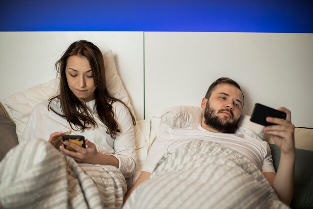 Donna castana e ragazzo barbuto guardando i loro smartphone