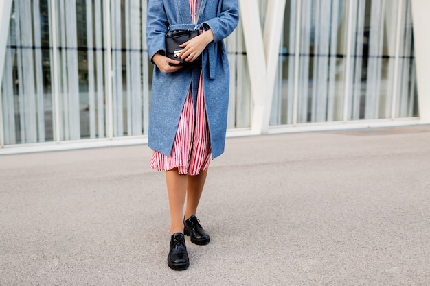 Donna castana felice in cappotto blu e vestito rosso che cammina lungo la strada moderna