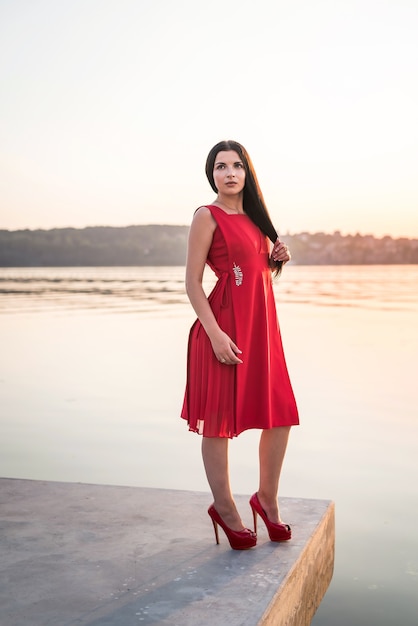 Donna castana in un vestito rosso in riva al mare