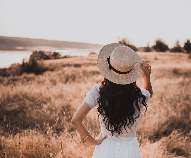 Donna castana in vestito bianco e cappello al tramonto