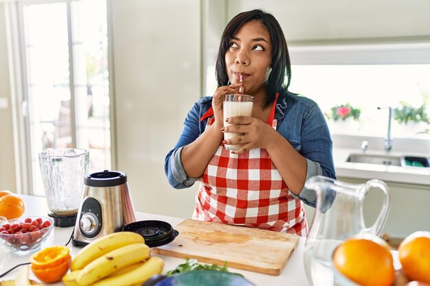 Donna castana ispanica che beve frullato di frutta fresca in cucina